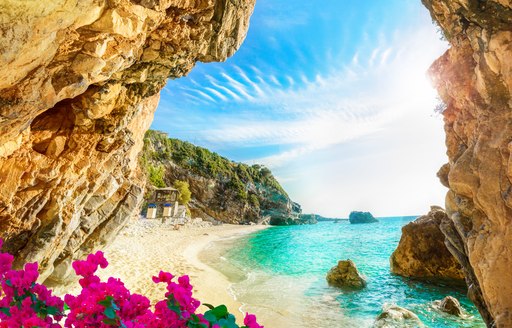View through a rock to a beautiful beach in Corfu Greece, with pink oleander flowers in the foreground