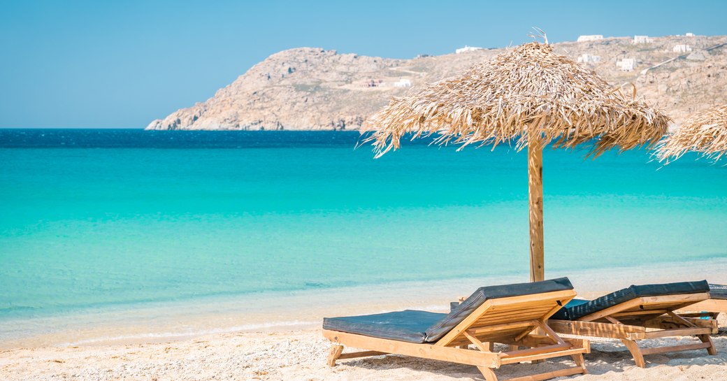A couple of sun loungers and thatched umbrella on a beautiful turquoise beach in Mykonos, Greece