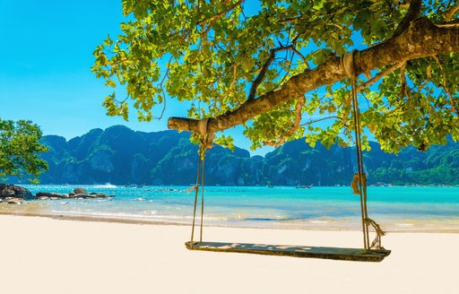secluded beach with a rope swing hanging from a tree in thailand