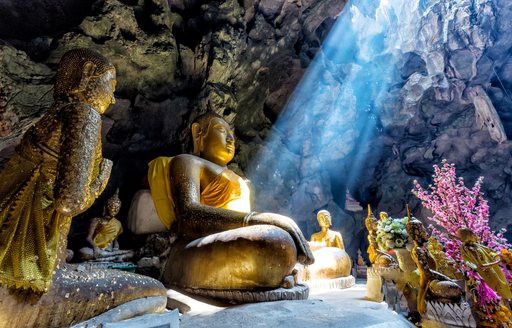 a buddha statue sits in a cave with sunlight streaming in from above in thailand
