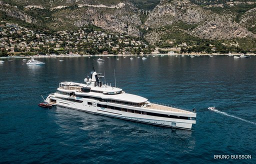 Feadship superyacht lady s underway in cinque terre in italy while on a luxury yacht charter vacation with a fleet of superyachts behind her