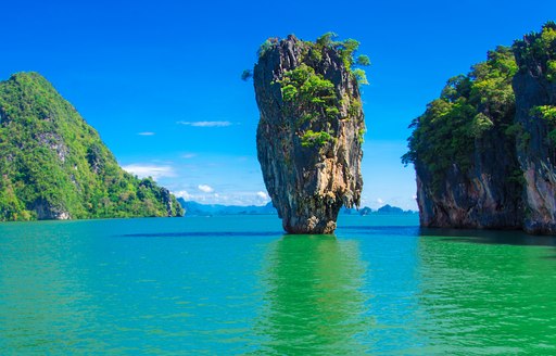 a towering rock sits in emerald waters in thailand