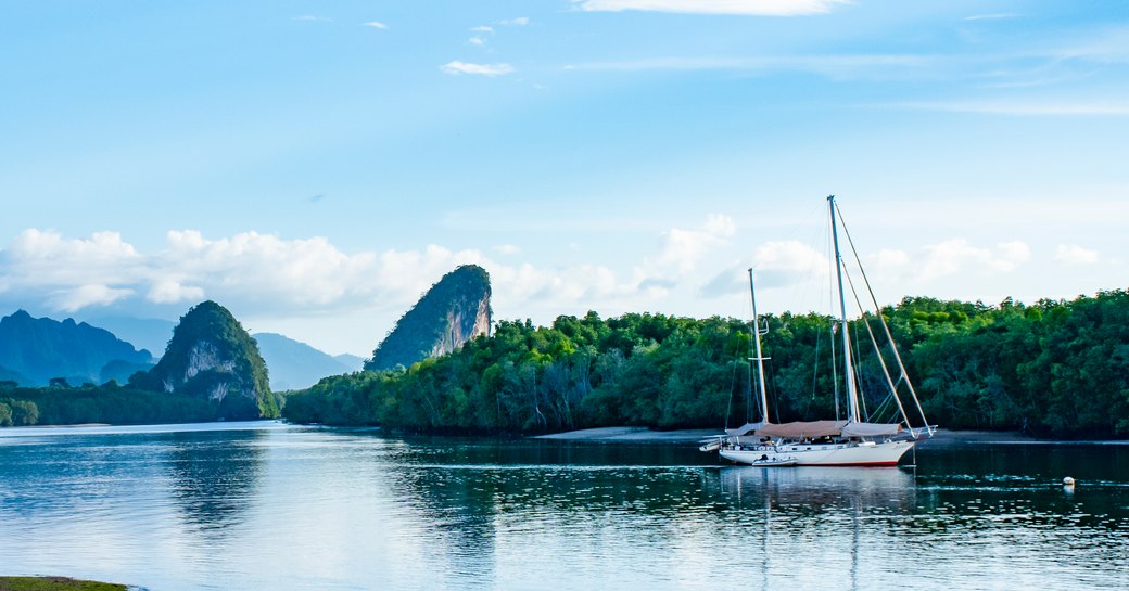 a sail yacht sits in the water in a bay in Thailand