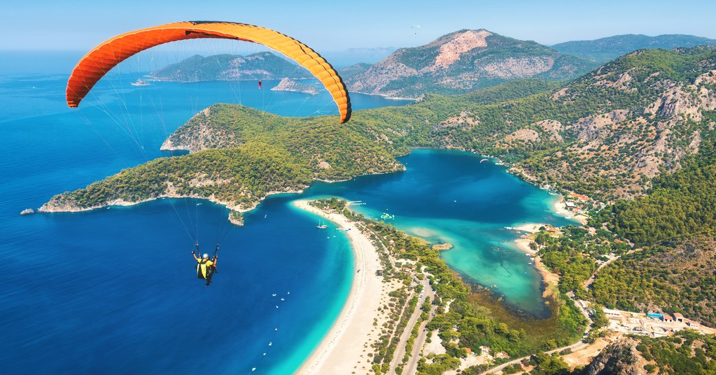 a guest on a luxury yacht charter who has anchored in oludeniz is paragliding over the breathtaking blue lagoon in turkey
