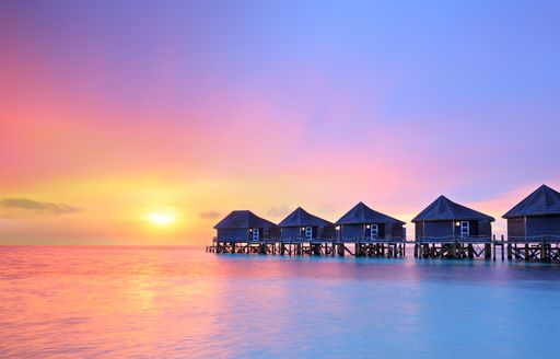 A series of wooden huts over the water in the Maldives at sunset