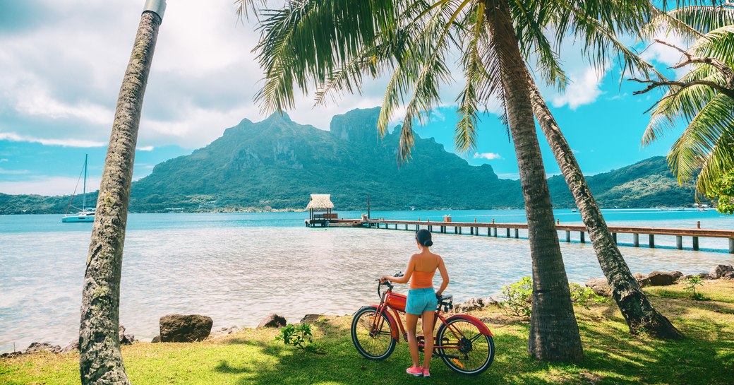 woman looking out towards the sea and mountains whilst holding a bike in Tahiti