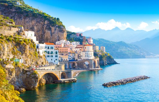 the  buildings of the amalfi coast nestled in the crevices of cliffs and hilltops with beautiful mountains in the background a perfect anchorage for guests on a superyacht looking to explore while on their italy yacht charter vacation 